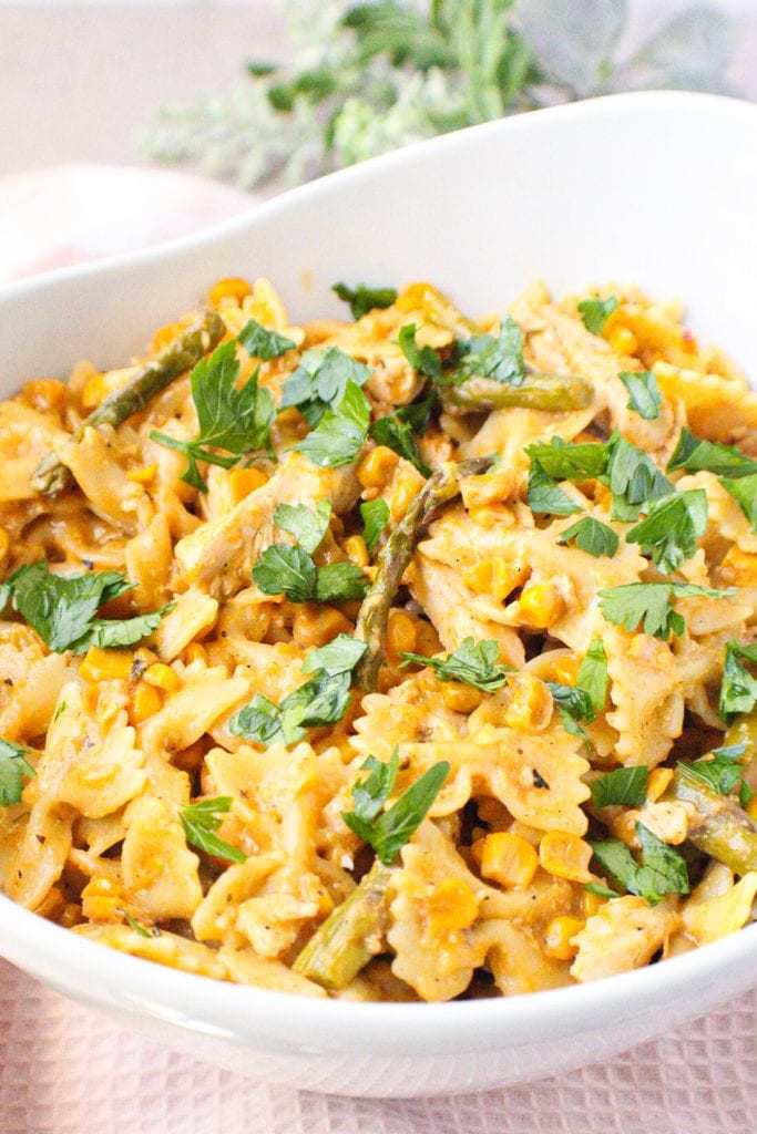 side angle shot of bowtie pasta with asparagus, corn and chicken in white serving bowl
