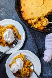 cornbread skillet peach cobbler in cast iron skillet with two servings on small plates