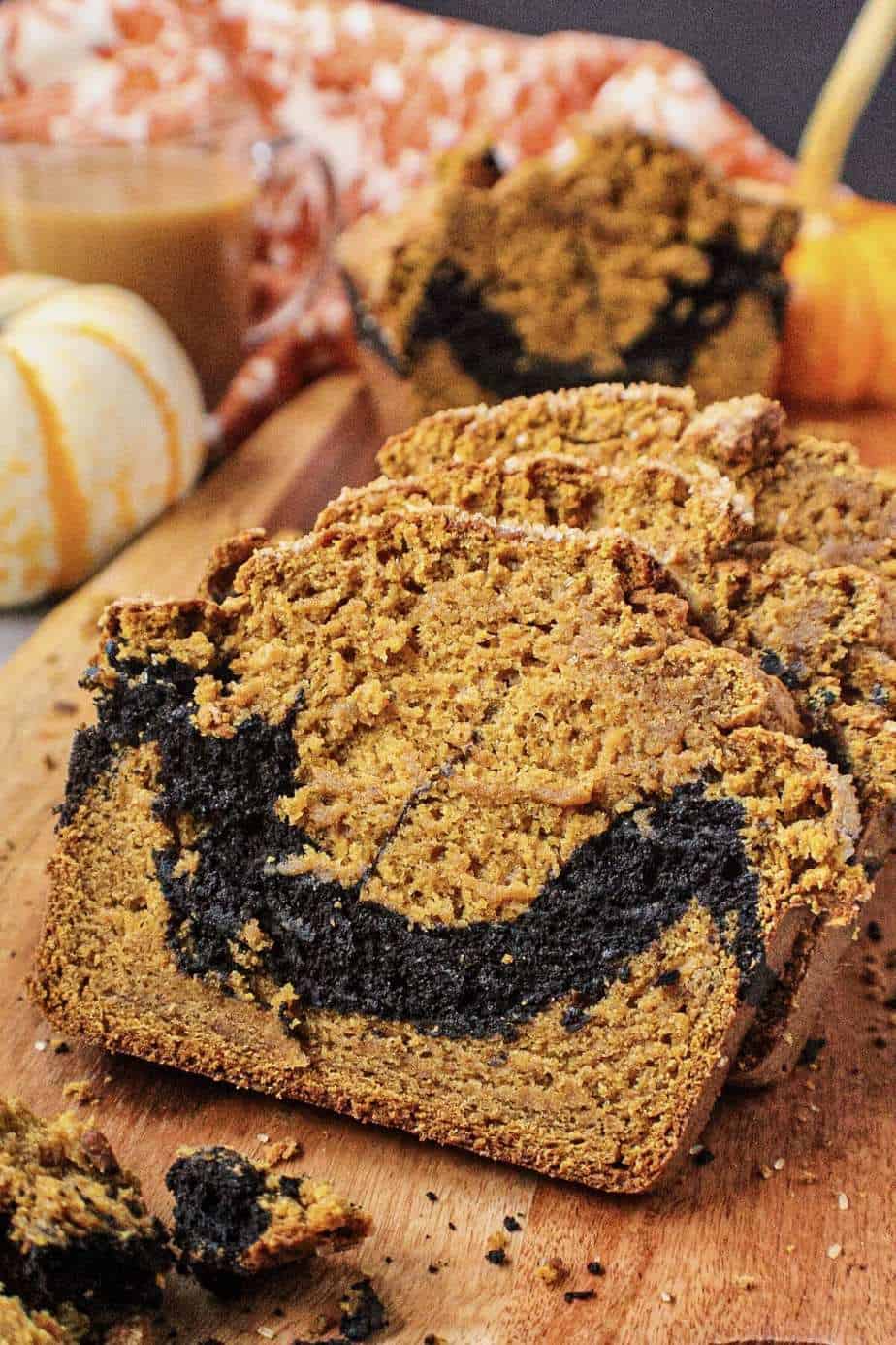side shot of chocolate marble pumpkin bread on wooden board with orange floral towel and pumpkins in shot perimeter