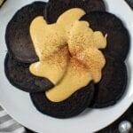 overhead shot of dark chocolate pancakes with pumpkin cream cheese glaze on white plate sitting on wooden surface