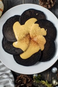 overhead shot of dark chocolate pancakes with pumpkin cream cheese glaze on white plate sitting on wooden surface