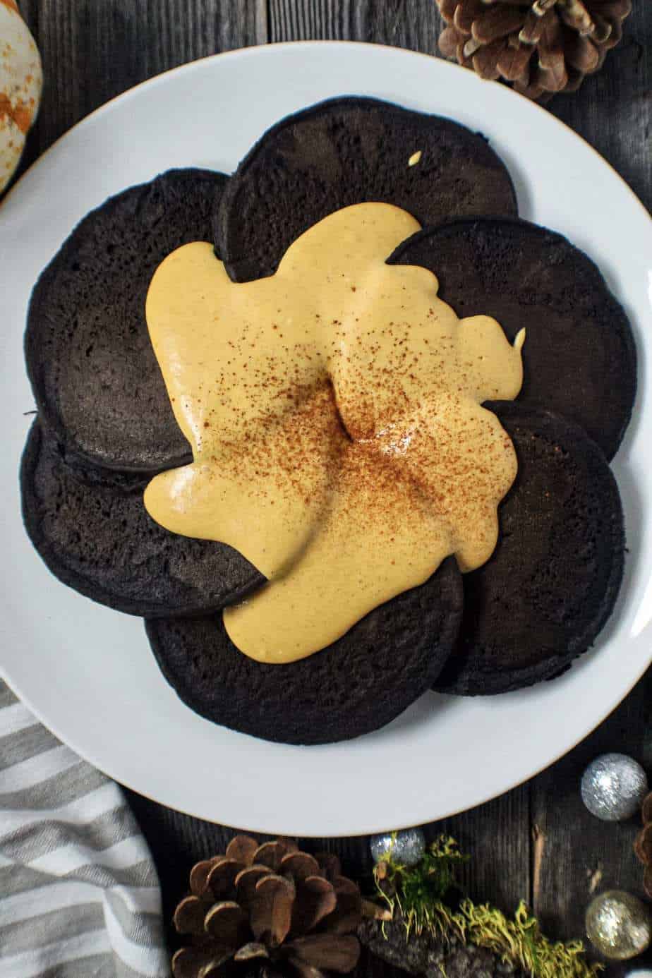 overhead shot of dark chocolate pancakes with pumpkin cream cheese glaze on white plate sitting on wooden surface