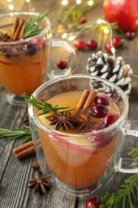 mulled apple cider served in clear mugs garnished with cinnamon sticks, star anise and cranberries on top of wooden surface