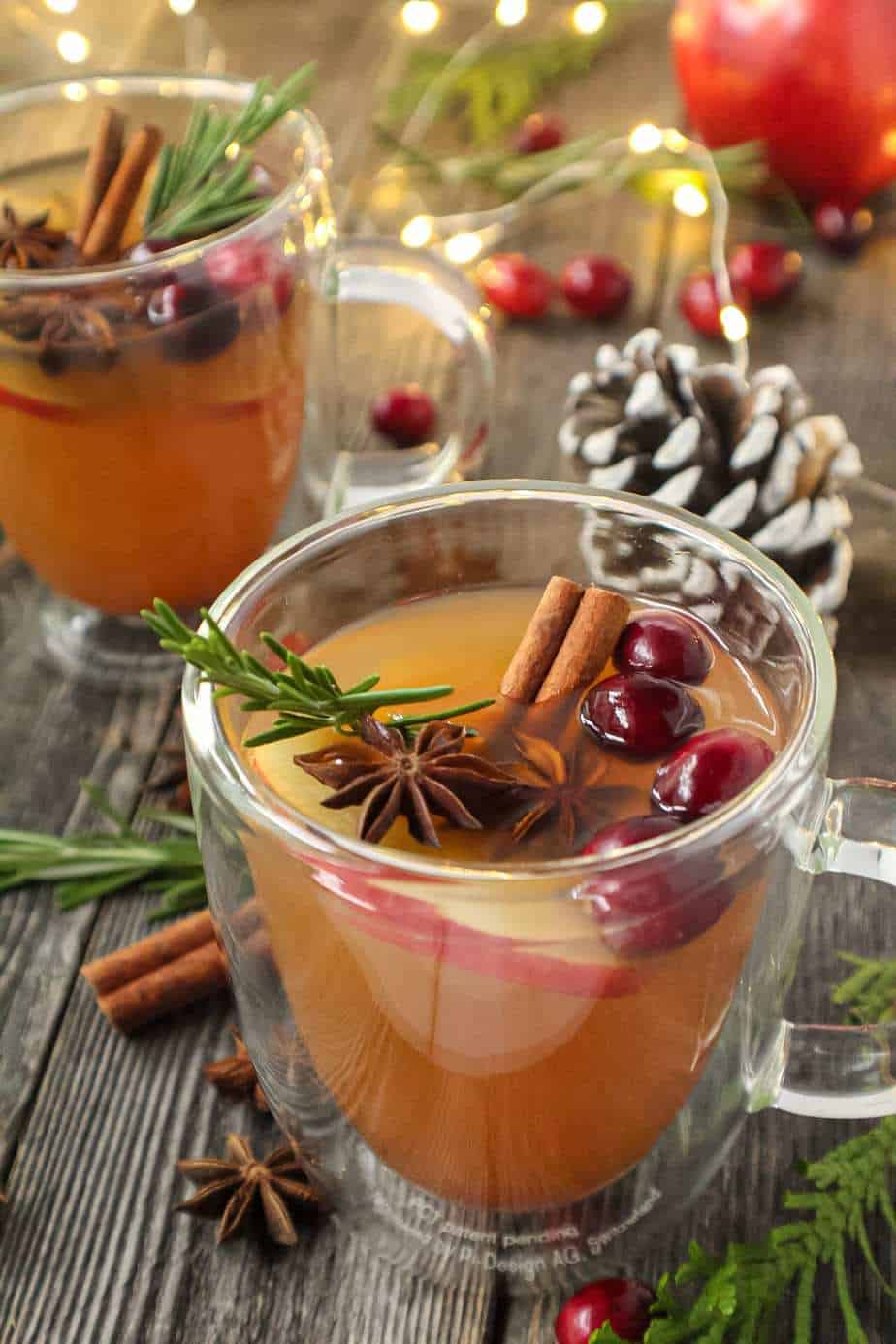 mulled apple cider served in clear mugs garnished with cinnamon sticks, star anise and cranberries on top of wooden surface