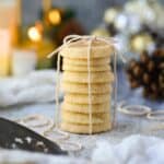Cardamom butter cookies stacked on a table with pinecones and candles in the background.