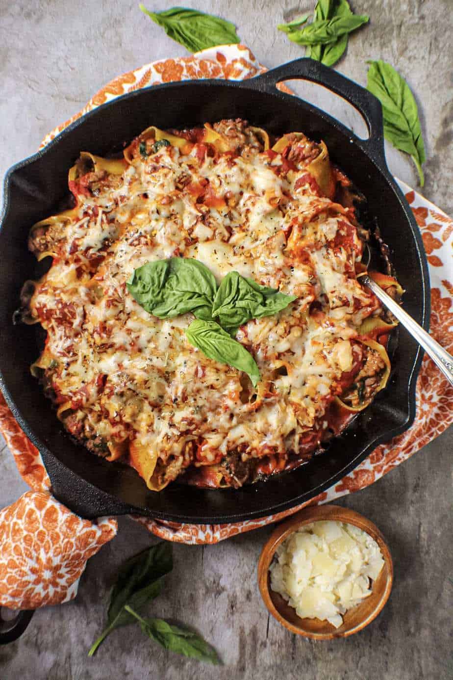 jumbo pasta shells stuffed with ground meat and tomatoes served in cast iron skillet and topped with cheese and fresh basil