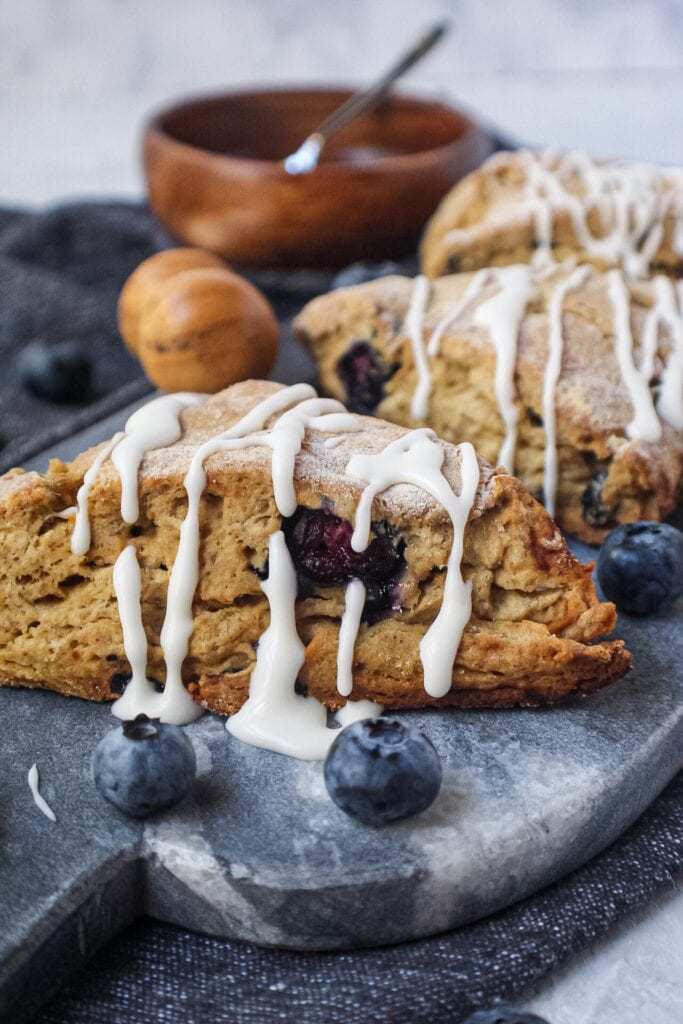 vegan blueberry scones with a powdered sugar glaze on a marble serving dish