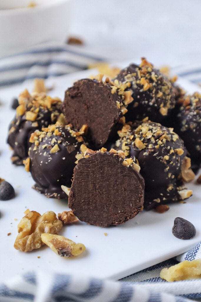 vegan dark chocolate truffles topped with chopped toasted walnuts on white plate with striped linen underneath plate
