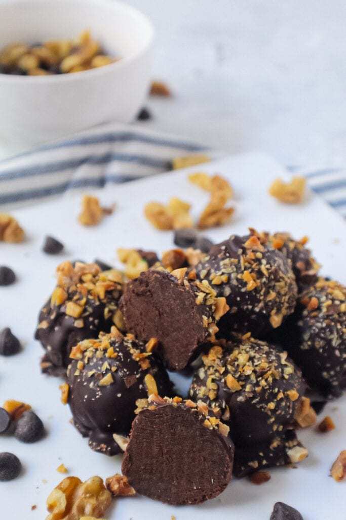 vegan dark chocolate truffles topped with chopped toasted walnuts on white plate with striped linen underneath plate
