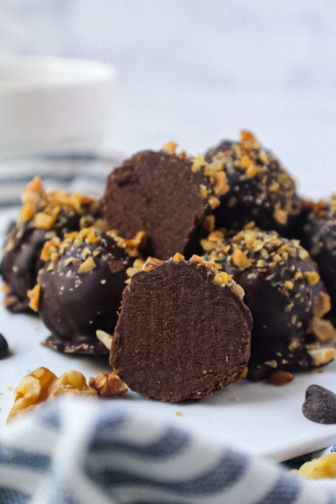 vegan dark chocolate truffles topped with chopped toasted walnuts on white plate with striped linen underneath plate
