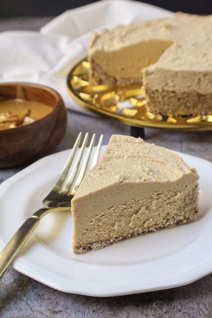 vegan peanut butter cheesecake on gold trivet with a slice of cheesecake on a small white plate with fork