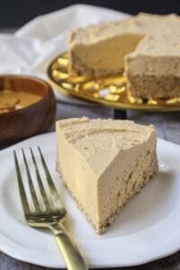 vegan peanut butter cheesecake on gold trivet with a slice of cheesecake on a small white plate with fork