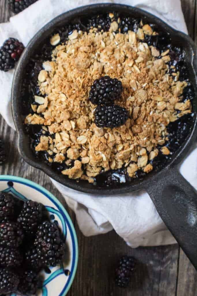 blackberry crumble with oat topping served in a 6-inch cast iron skillet topped with fresh blackberries.