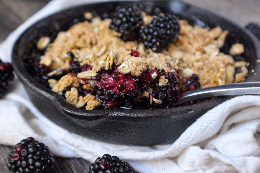 blackberry crumble with oat topping served in a 6-inch cast iron skillet topped with fresh blackberries.