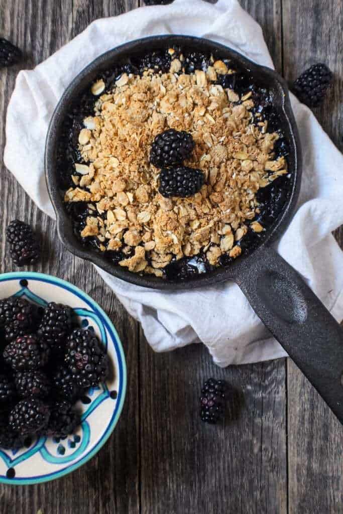 blackberry crumble with oat topping served in a 6-inch cast iron skillet topped with fresh blackberries.