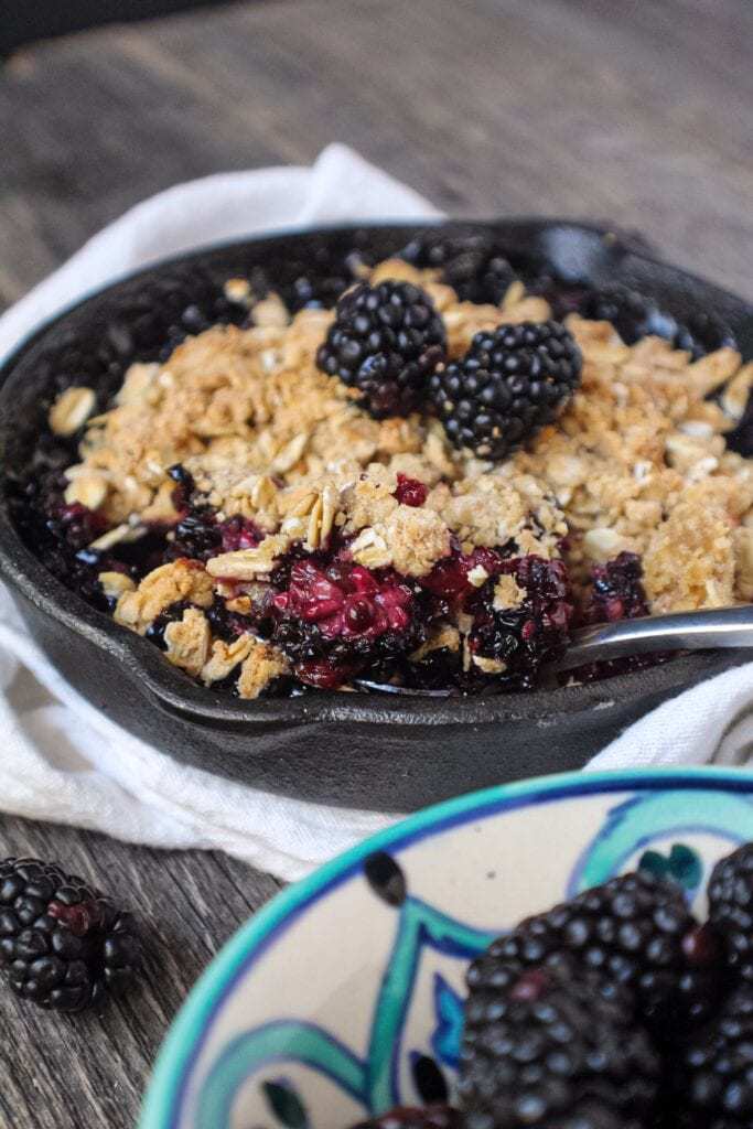blackberry crumble with oat topping served in a 6-inch cast iron skillet topped with fresh blackberries.
