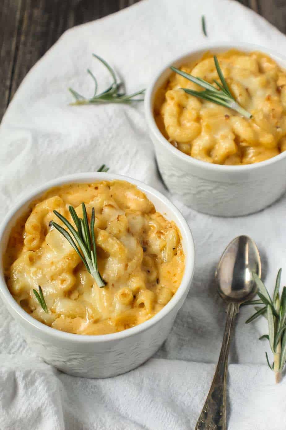 smoked cheddar mac and cheese served in two single-serve ramekins sitting on top of white linen topped with fresh rosemary and a small spoon beside ramekin.