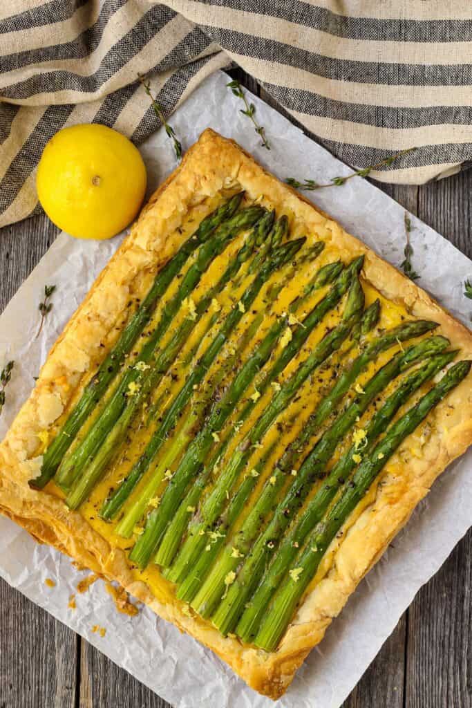overhead shot of asparagus tart on wooden surface with half a lemon a striped linen in perimeter of shot