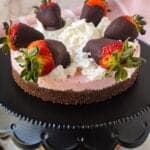 chocolate strawberry no-bake cheesecake on cake stand topped with whipped cream and strawberries