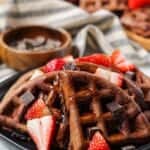 side angle shot of Double dark chocolate strawberry waffles topped with dark chocolate chunks, pancake syrup and sliced strawberries