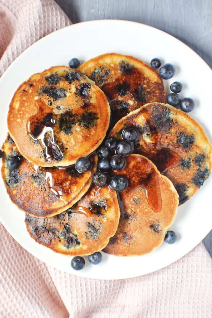 overhead shot of almond flour pancakes on white dinner plate with fresh blueberries