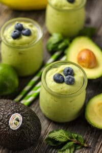 side shot of avocado smoothis on wood surface topped with fresh blueberries