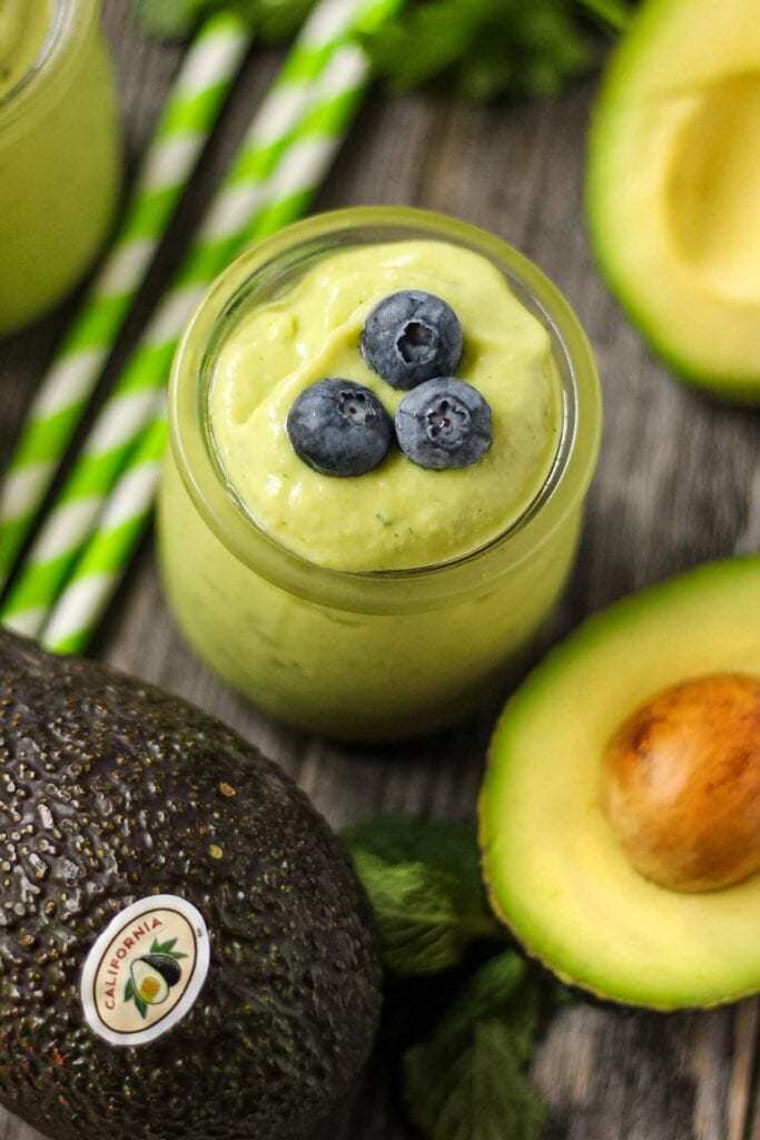 close up of tropical avocado smoothie in clear glass with fresh avocados in perimeter. 