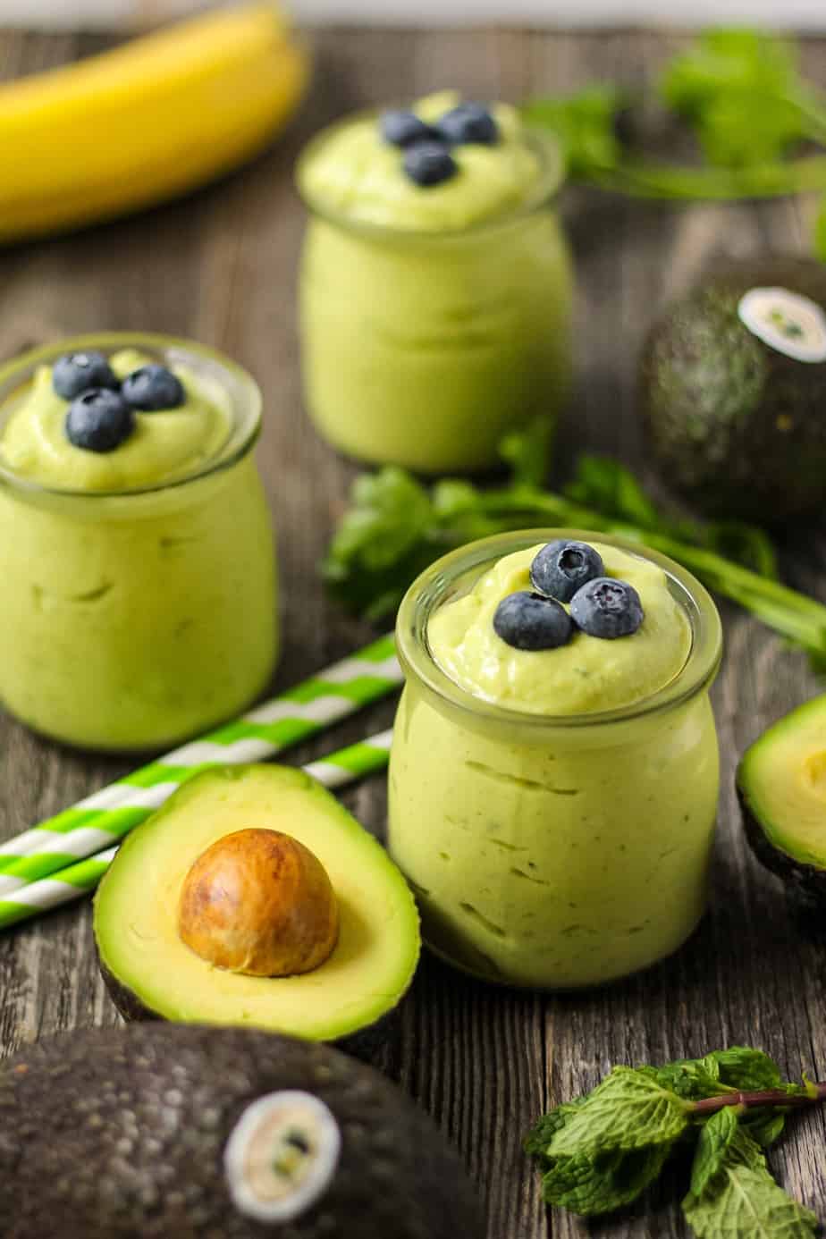 side shot of tropical avocado smoothies with fresh avocados in perimeter of shot