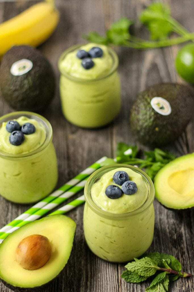 side shot of tropical avocado smoothies on wooden surface with fresh avocados in perimeter of shot