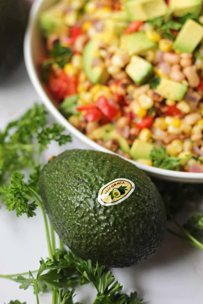 close up of avocado with succotash in the background
