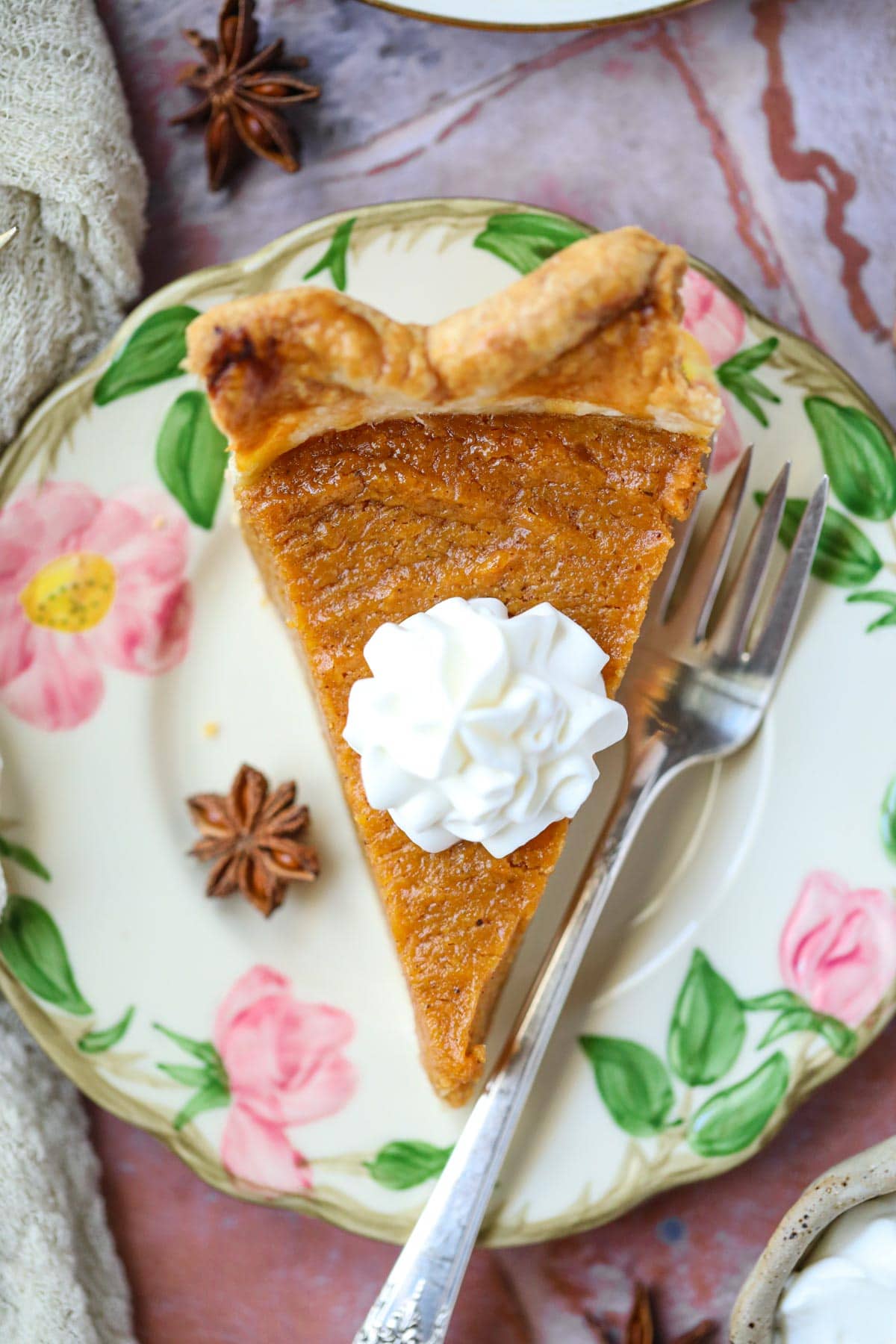 A slice of black folks southern sweet potato pie topped with fresh whipped cream on a dessert plate.