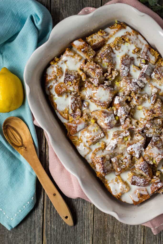 overhead shot of lemon bread pudding with greek yogurt glaze on wooden surface with wooden spoon and lemon in perimeter of shot
