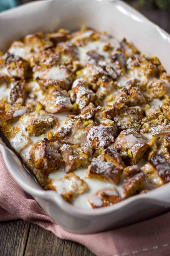side shot of lemon bread pudding with lemon greek yogurt glazein glass baking dish on wooden surface.