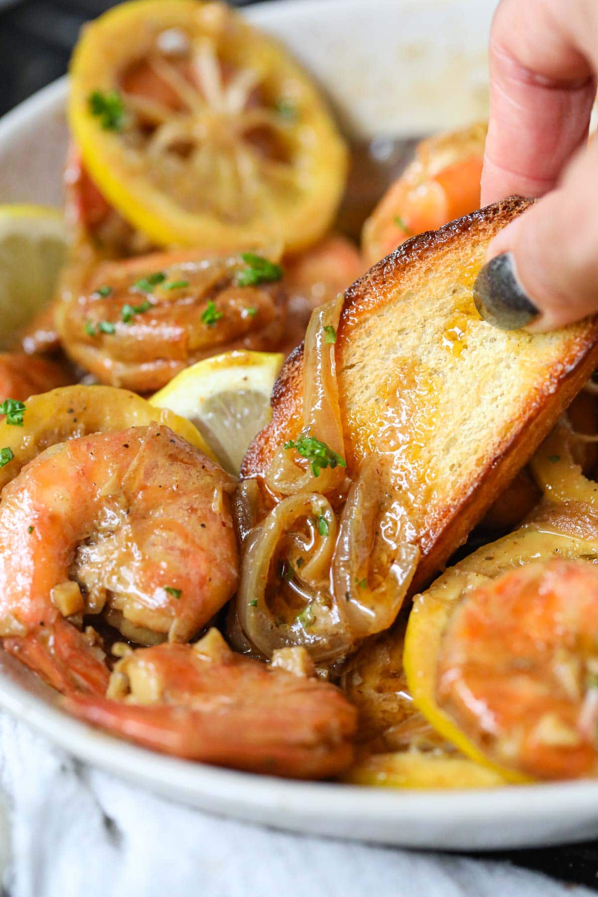 A slice of toasted bread being dipped into a bowl of New Orleans barbecue shrimp.
