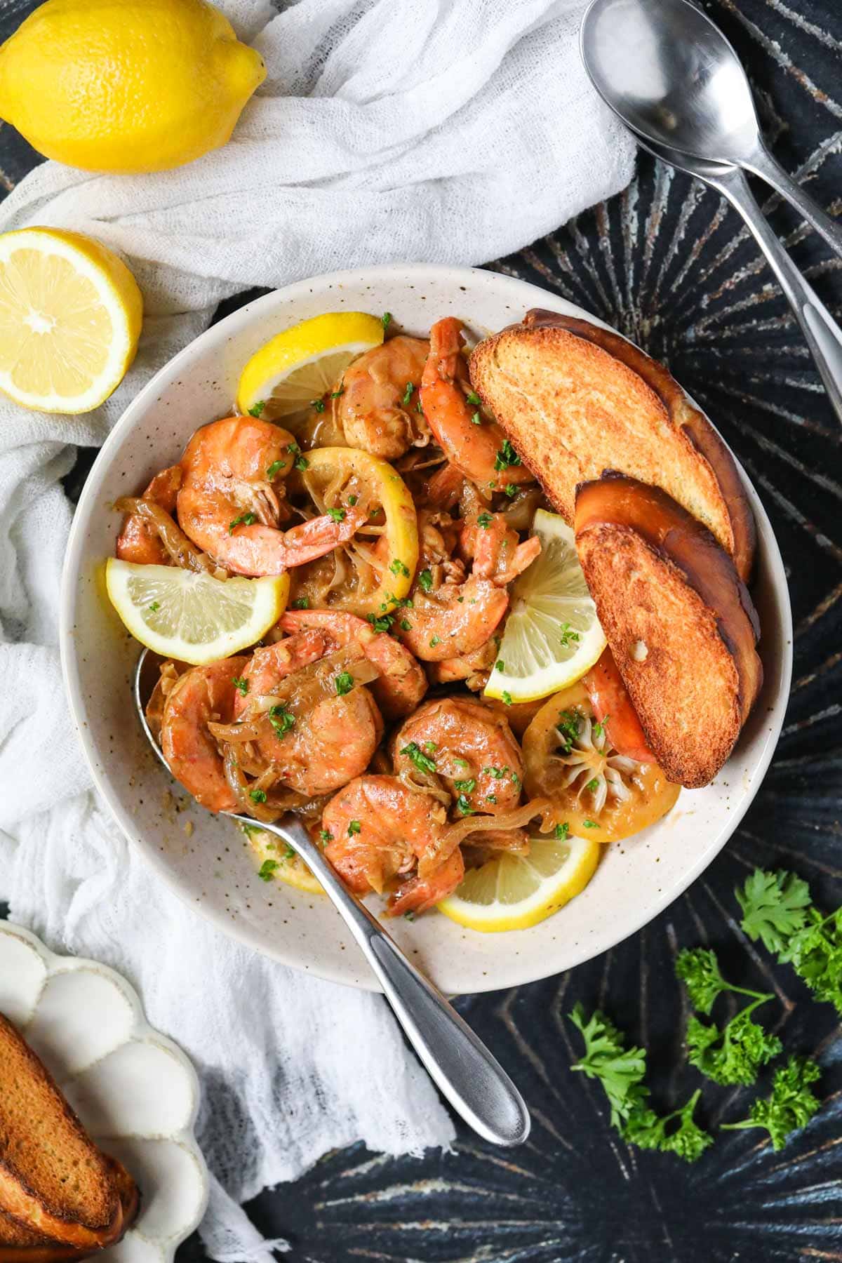 New Orleans barbecue shrimp in a white bowl sitting on top of a black surface.