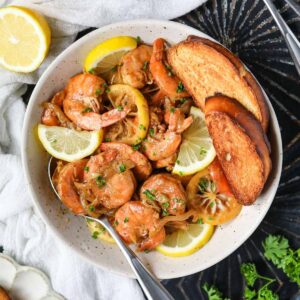 New Orleans barbecue shrimp in a white bowl sitting on top of a black surface.