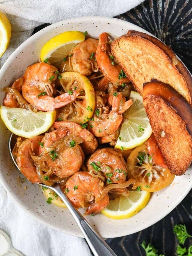 New Orleans barbecue shrimp in a white bowl sitting on top of a black surface.