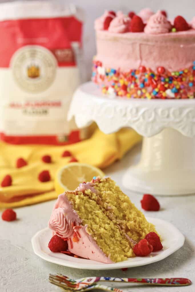 side shot of lemon raspberry birthday cake on cake stand with bag of flour in the background