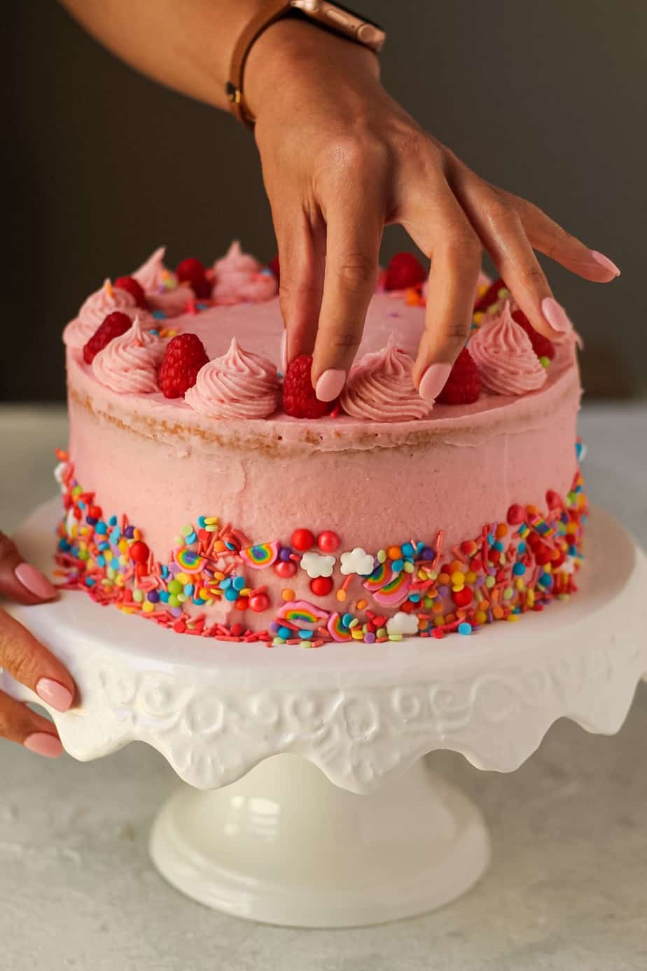 hand placing raspberry on lemon raspberry birthday cake
