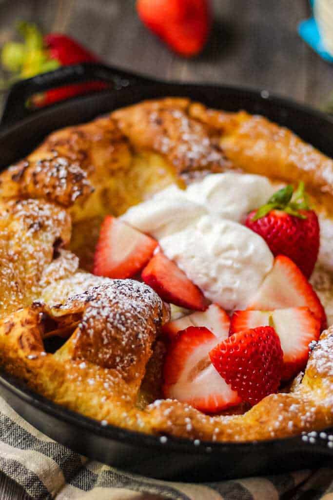 close up side shot of roasted strawberry dutch baby in cast iron skillet on wooden surface