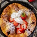 overhead shot of roasted strawberry dutch baby in cast iron skillet on wooden surface