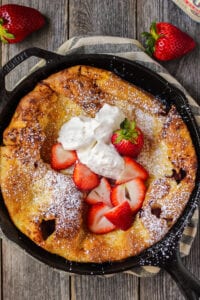 overhead shot of roasted strawberry dutch baby in cast iron skillet on wooden surface