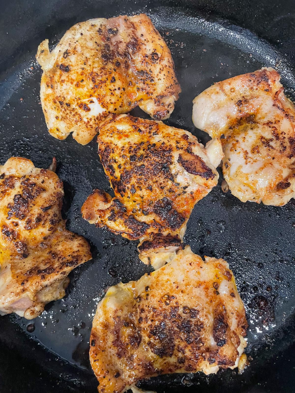 chicken thighs cooking in cast iron skillet