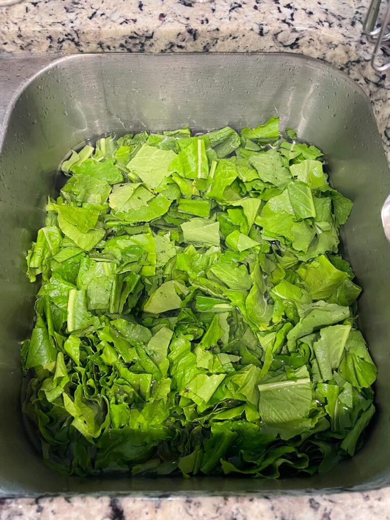 chopped turnip greens being cleaned in a kitchen sink.
