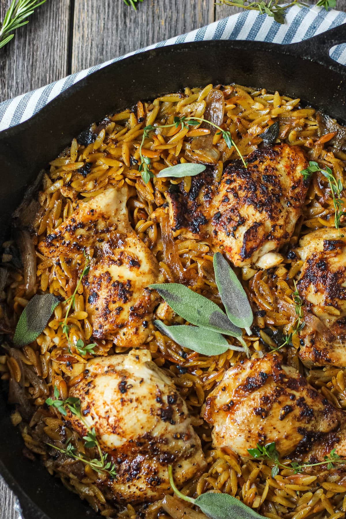 overhead close up shot of one pan sage butter chicken and orzo in a cast iron skillet on wooden surface