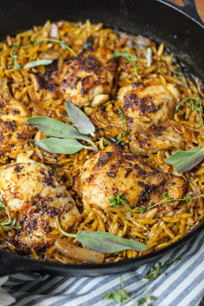 close up side angle shot of one pan sage butter chicken and orzo in a cast iron skillet on wooden surface
