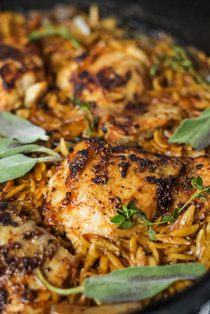 detailed shot of one pan sage butter chicken and orzo in a cast iron skillet on wooden surface