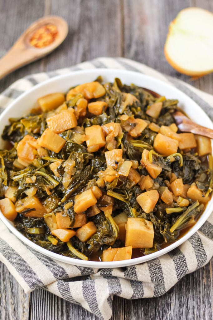 side angle shot of sweet and spicy turnip greens in white bowl on wooden surface.