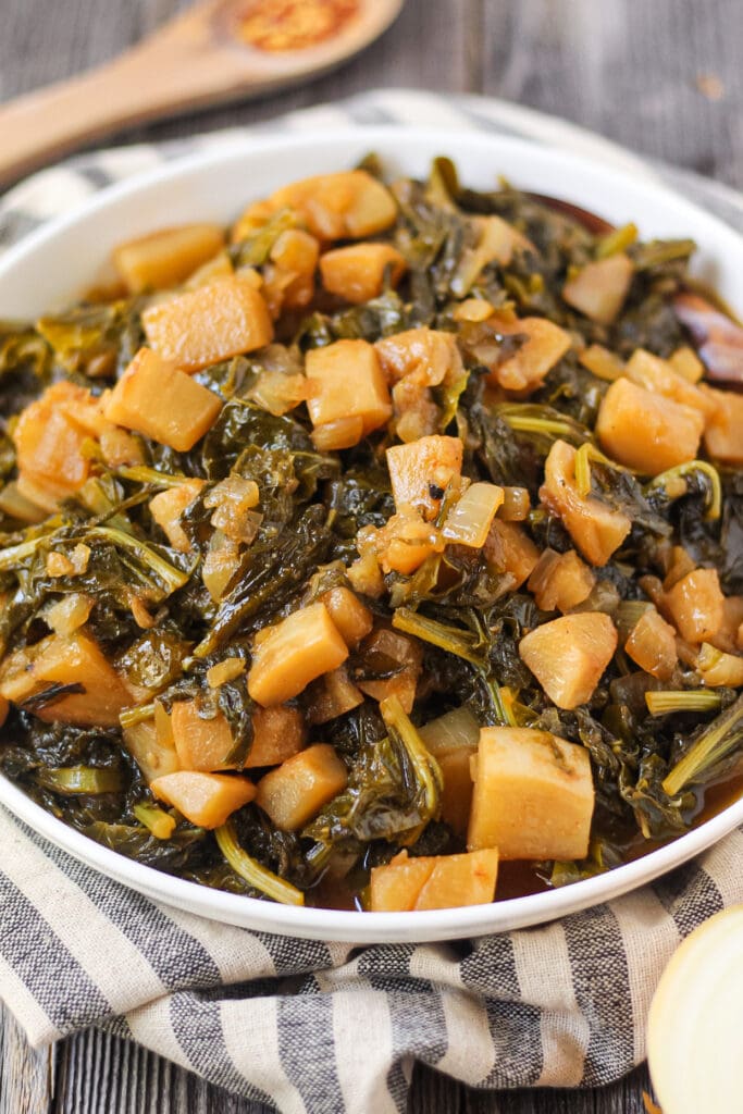side angle shot of sweet and spicy turnip greens in white bowl on wooden surface.