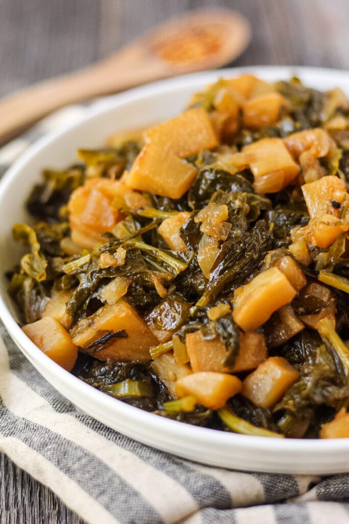 close up shot of sweet and spicy turnip greens in white bowl on wooden surface.